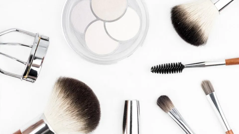 Bløde makeuppensler og en pudderdåse på lys baggrund